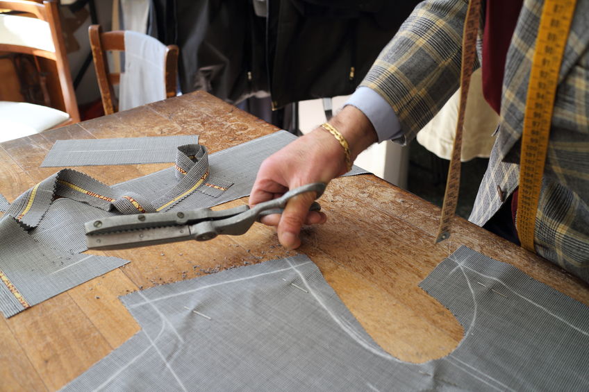 Hand holding special scissors for cutting suit fabric above pieces of cut up suit fabric.